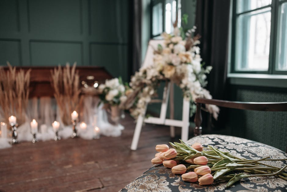 A person dressed in a dark coat holding a bouquet of white lilies with long green leaves, set outdoors near a cemetery with headstones and grass in the background, under natural daylight, showcasing f